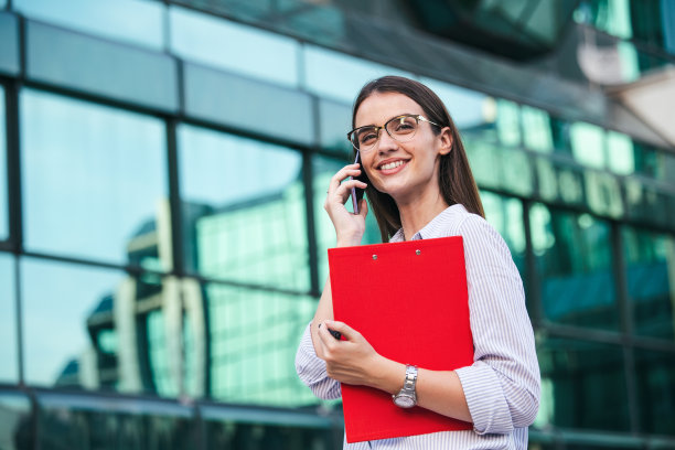 快乐美丽的商务女人与剪贴板通话的手机。成功商业女性的肖像拿着剪贴板。照片中的女商人穿着西装，手里拿着文件。图片下载