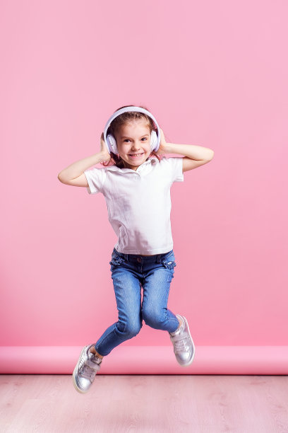 女孩戴着耳机在听粉色背景的音乐。跳舞的女孩。快乐的小女孩随着音乐跳舞。可爱的孩子享受快乐的舞蹈音乐图片下载