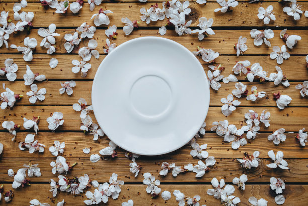 桌子中央放着一个白色的空盘子，周围是盛开的杏花，背景是旧的棕色。图片下载