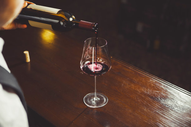 特写照片，侍酒师在吧台背景上倒红酒到杯子里。图片下载