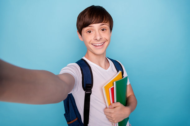 这张照片是一个快乐的好男孩在他上学的路上拍摄自己，而他被孤立在蓝色的背景下图片下载