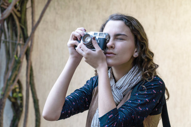 年轻漂亮的女孩拍照与数码复古相机在花园在阳光明媚的夏天与清楚的墙背景。旅行、艺术、自由、摄影、青春和科技理念。图片下载