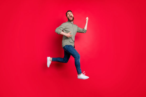 全身照片的愉快好玩快乐愉快英俊的白色时尚模特摇滚音乐家穿着灰色衬衫想象像弹吉他，而孤立与红色背景图片下载