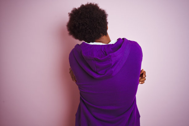 年轻的非洲裔美国人穿着紫色的运动衫站在孤立的粉红色背景下，从后面高兴和积极地拥抱自己。爱自己，关心自己图片下载