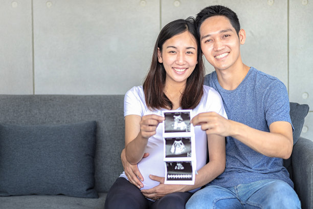 超声波怀孕的妈妈和爸爸。开心的孕妇带着丈夫展示自己宝宝的扫描图。幸福的夫妇正拿着宝宝的超声波照片。图片下载