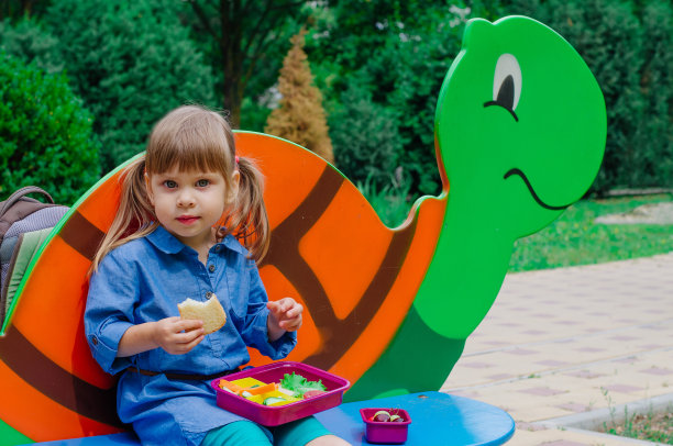 微笑的女学生坐在户外吃午餐盒里的午餐图片下载