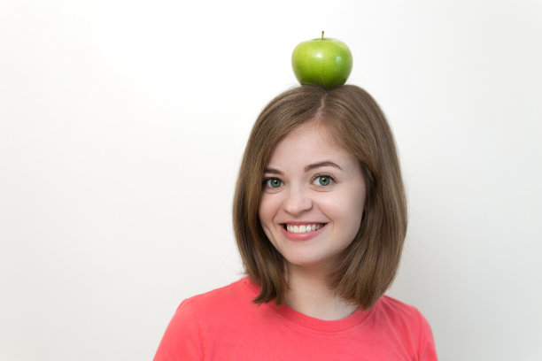 微笑的白人妇女女孩的肖像与绿色苹果在她的头。健康的生活方式，水果素食饮食。图片下载