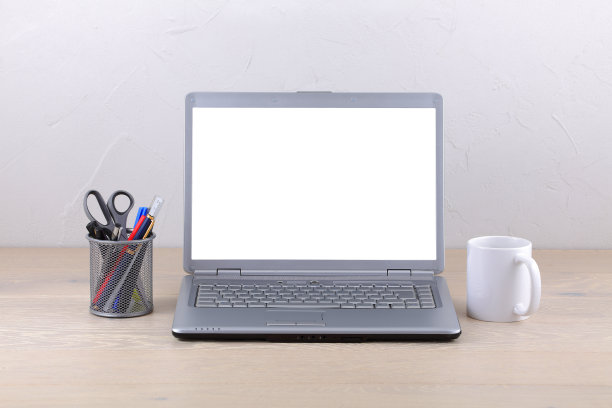 办公桌上有一台笔记本电脑，咖啡杯和笔。带有剪切路径的白屏幕模板图片下载