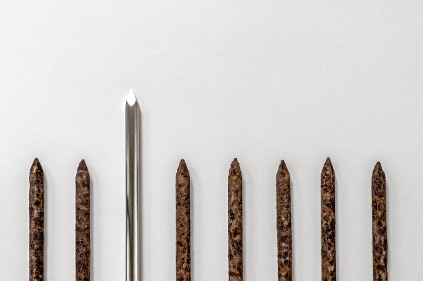 金属闪亮锋利的钉子突出在一排老生锈的钉子在一个明亮的背景。图片下载