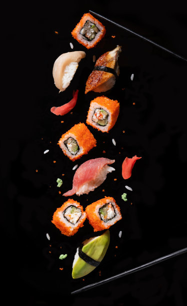 寿司片夹在筷子之间，在黑色的背景上飞散。图片下载