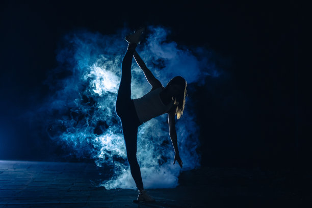 在黑暗的背景中，那个女人在烟雾中做着垂直的分裂图片下载