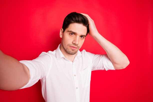 大男子主义英俊男子的自画像，录制关于头发护理的视频，而孤立的红色背景图片下载