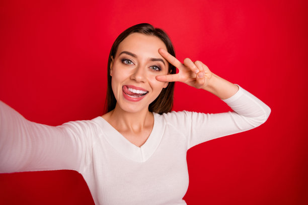 迷人的迷人的美丽的女人诱惑你的照片通过相机显示v标志，而孤立与红色背景图片下载