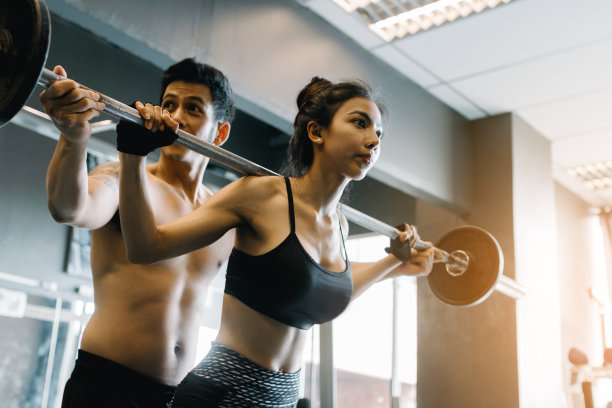 私人教练帮助女性和处理沉重的杠铃在健身房的肩膀上。图片下载
