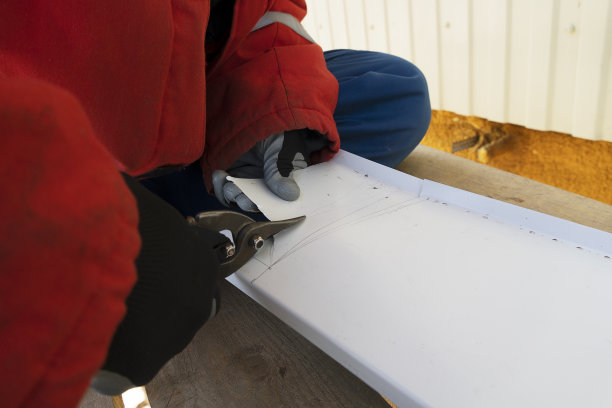 一个戴着手套的工匠正在用剪刀剪一块白色的钢板。一个正在工作的锡匠在一个记号处切铁。图片下载