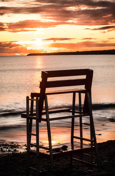 日出时，救生员坐在海滩上图片下载