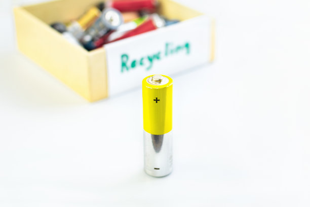 一节AA电池放在一个装有废旧电池的盒子前面，上面写着“回收”字样，准备好正确处理对环境和土壤有毒的物质。图片下载