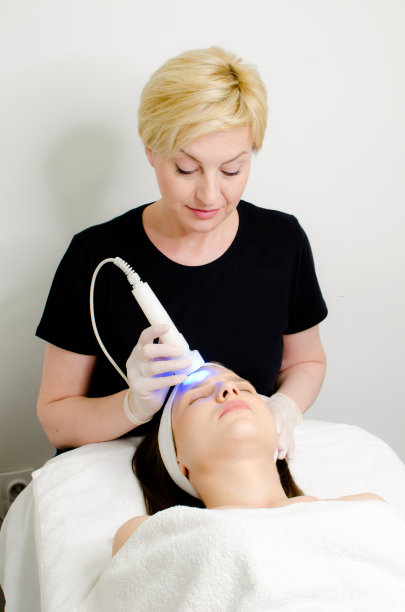 美容师在美容院对女性顾客使用蓝光疗法，面部光疗对皮肤毛孔进行清洁图片下载
