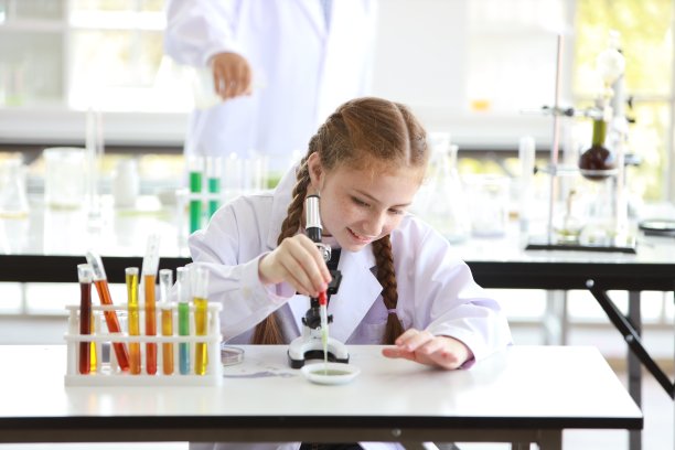好奇的小女孩开心地用显微镜和笑脸做科学实验(教育和科学概念)图片下载