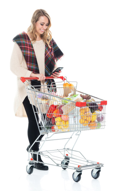 年轻漂亮的女人推着购物车，用手机发短信图片下载