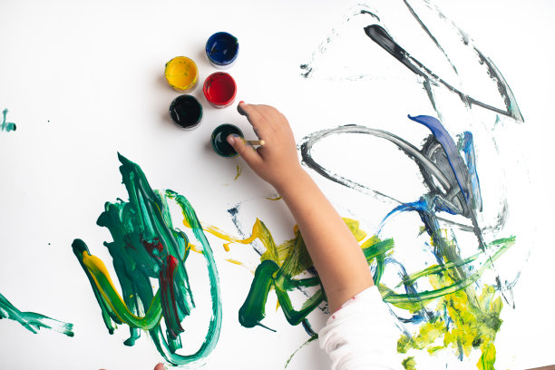 一个小男孩的手在白纸上用水彩画。小男孩拿着画笔和颜料。回到学校的概念。Copyspace。图片下载