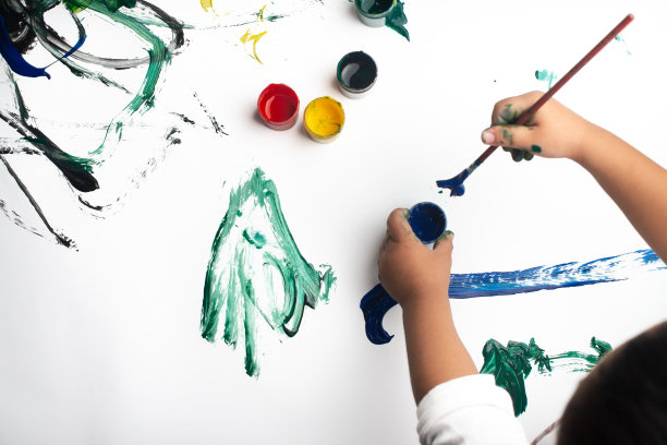 一个小男孩的手在白纸上用水彩画。小男孩拿着画笔和颜料。回到学校的概念。Copyspace。图片下载