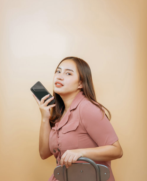 亚洲女子坐在椅子上，拿着手机，背景是橙色。复制版面放置广告。图片下载