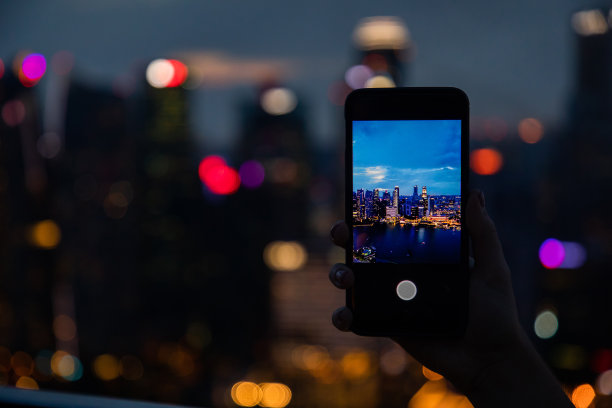 女人拿着手机，从新加坡滨海湾金沙豪华酒店屋顶拍摄天际线的照片图片下载