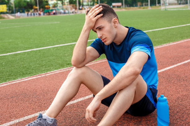 有休息。一个年轻人在体育馆外面坐着，头上靠着一瓶水，累了图片下载