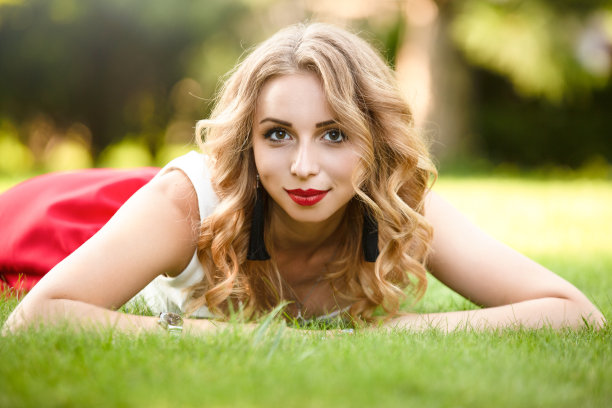 俯视图有吸引力的女性模特躺在公园的绿色草地上，在休息的时间看相机，高加索女人与金发花一天在自然的肖像图片下载