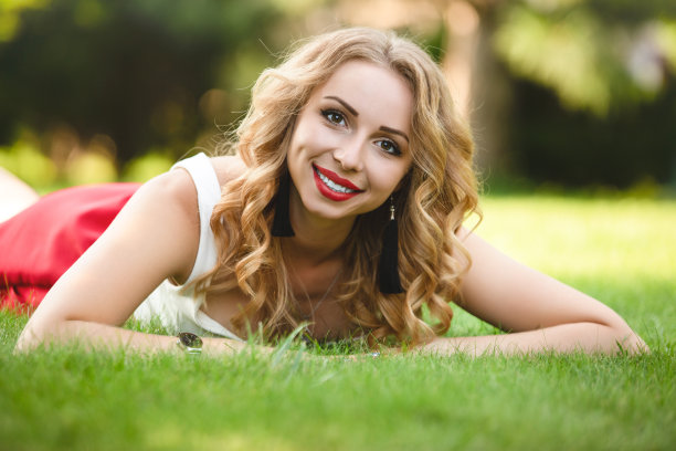 俯视图有吸引力的女性模特躺在公园的绿色草地上，在休息的时间看相机，高加索女人与金发花一天在自然的肖像图片下载