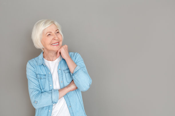 资深女子在牛仔夹克工作室孤立在灰色的墙壁上看着一边快乐图片下载