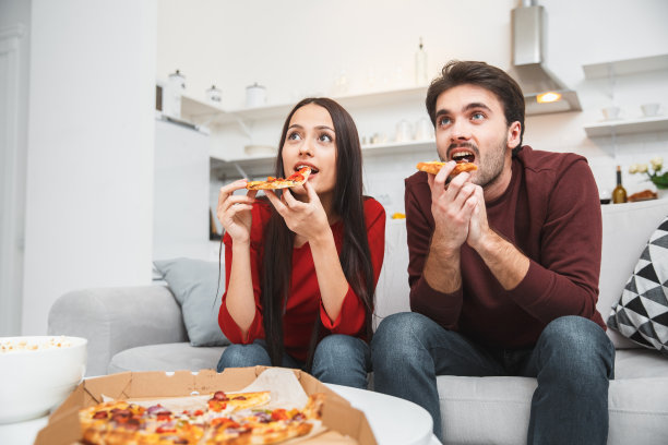 年轻夫妇在家里享受浪漫的夜晚，吃披萨看电视图片下载