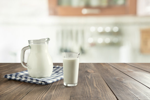 木桌上放着新鲜牛奶和水壶，背景是模糊的厨房。图片下载