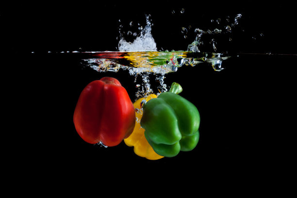 黄色、绿色和红色的辣椒落入水中，溅起黑色的水花图片下载