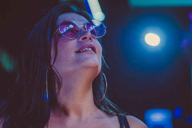 戴着眼镜的年轻美丽的千禧女孩在街上霓虹灯的背景下拉直她的头发。街的照片。图片下载