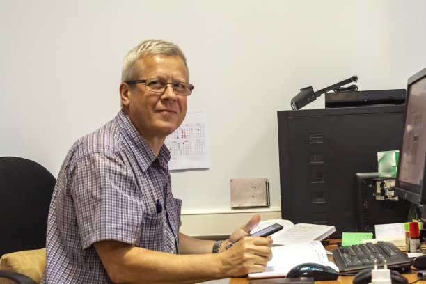 笑容可掬的老人坐在台式电脑旁边。老人在工作图片下载