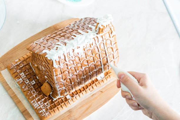 准备圣诞节，迎接新年。传统圣诞姜饼屋的烹饪和装饰，照片中女性的手，俯视图，白色背景图片下载