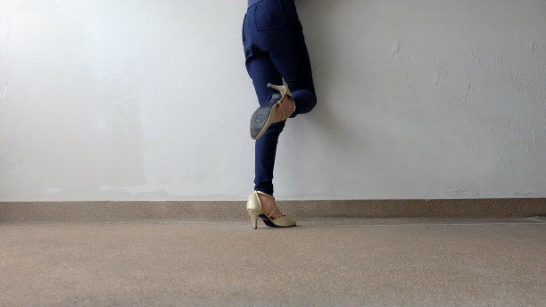 高跟鞋。时尚的年轻女子穿着蓝色裤子和金色高跟鞋在街道道路的背景。图片下载