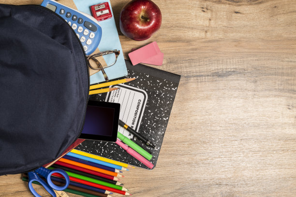 回到学习用品，背包放在木制的学生书桌上。图片下载