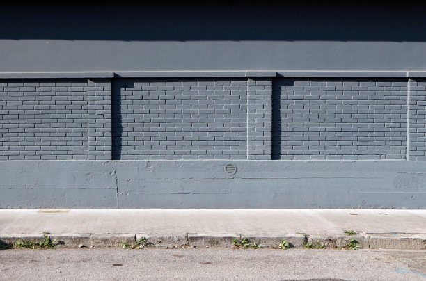 混凝土和砖墙刷成灰色，前面是人行道和柏油路。图片下载