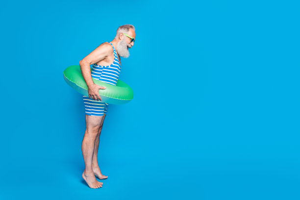 全身侧面照片惊讶的男子低头看他的眼镜，戴着绿色的救生衣，穿条纹泳衣孤立在蓝色的背景图片下载