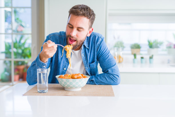 帅哥在家对着镜头微笑着吃着肉丸和番茄酱意大利面图片下载