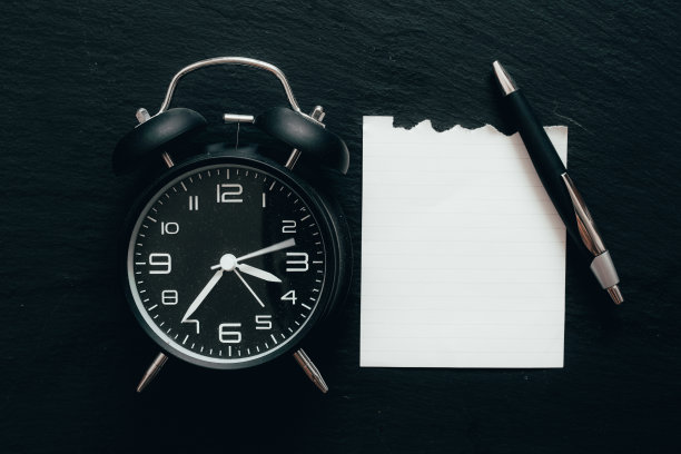 旧闹钟旁边的一张纸和一支笔在黑色的背景上图片下载