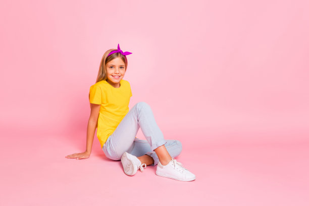 她的肖像，她漂亮迷人，可爱的，愉快的，愉快的十岁前的女孩穿着黄色的t恤坐在地板上chill out花空闲时间孤立在粉红色的柔和的背景图片下载