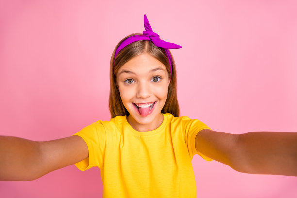 她的自画像，她漂亮迷人，可爱的疯狂，愚蠢，顽皮，快乐，愉快的十岁前的女孩穿着黄色的t恤，愚弄，有乐趣，自由时间孤立在粉红色的柔和的背景图片下载