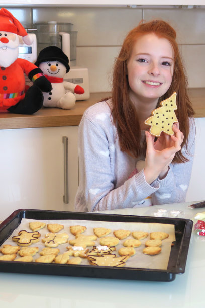 14 / 15岁的红发少女穿着白色衣服，现代厨房里展示着她用糖霜装饰的圣诞饼干图片下载