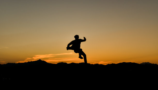 一个跳跃的男人在日落的剪影，概念生活方式自由度假旅行。图片下载
