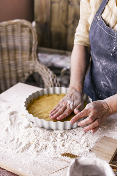 女性的手，面粉，面团和一个蛋糕盘。一个穿着围裙的妇女正在为家庭烘焙准备生面团。乡村风格的照片。木桌，麦穗和面粉。情感上的照片。舒适的气氛。图片下载