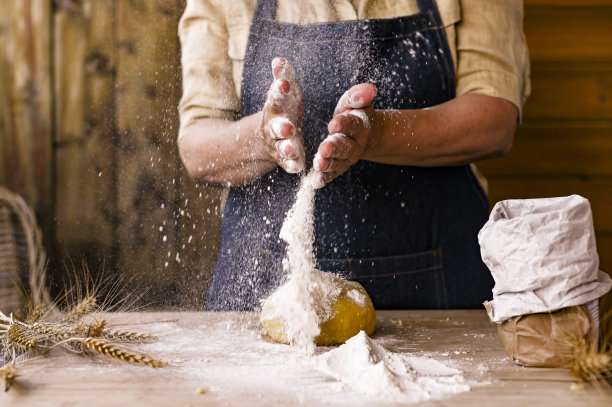 女人的手，面粉和面团。在面团和面粉的框架中悬浮。一个穿着围裙的妇女正在为家庭烘焙准备生面团。乡村风格的照片。木桌，麦穗和面粉。情感上的照片。图片下载